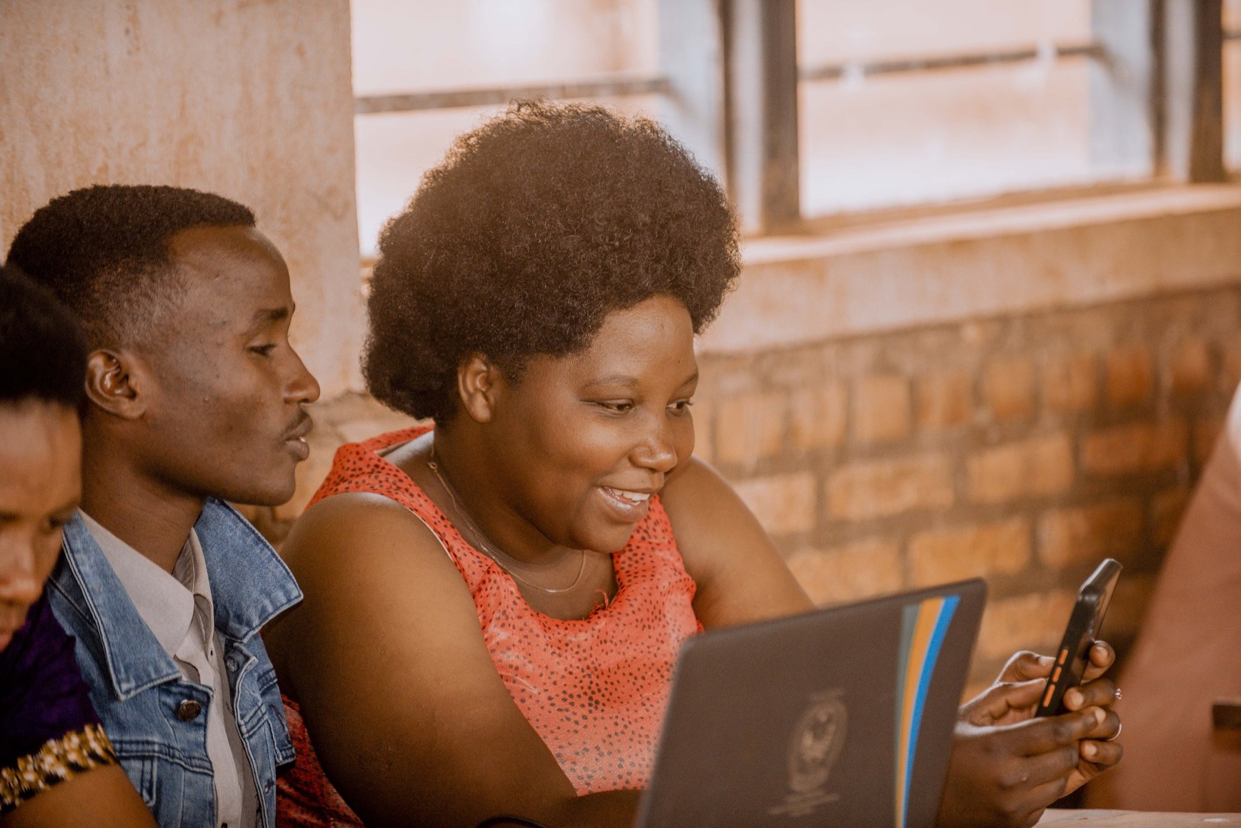 Two young people looking at a laptop and a phone together